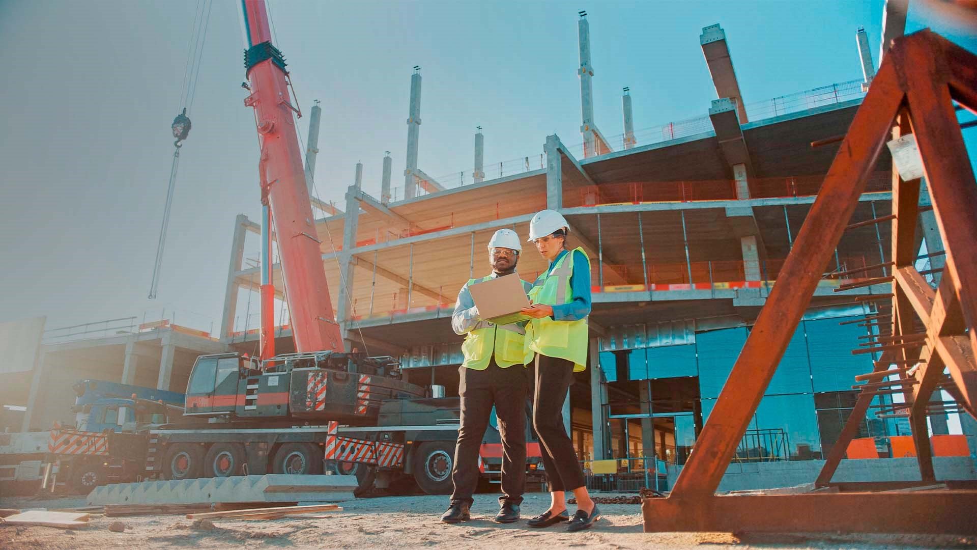 Chefs de projet, homme et femme discutant devant un ordinateur avec un chantier résidentiel derrière et un camion nacelle.