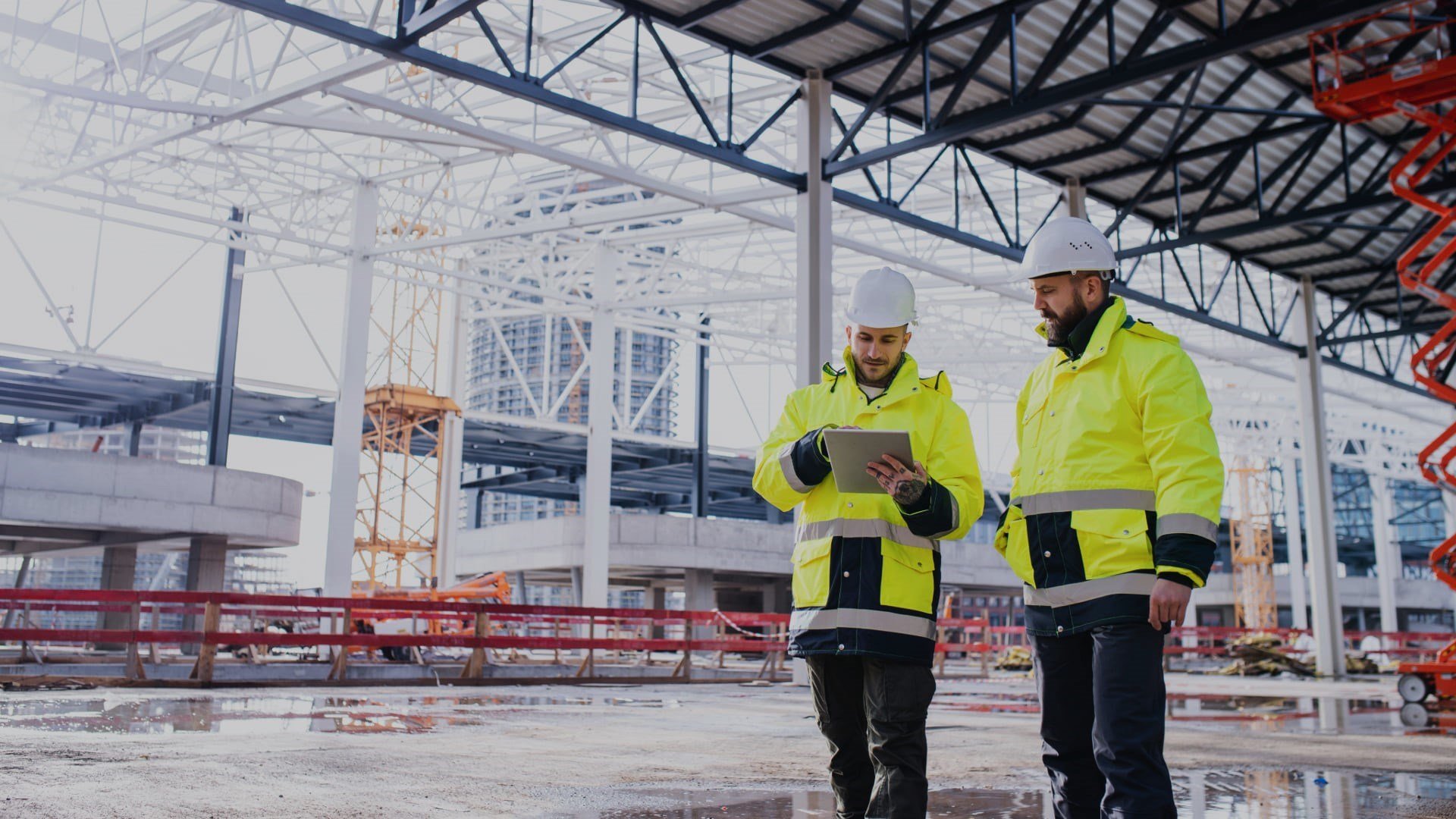 Photo de deux chefs de projets travaillant sur un chantier en construction avec une plateforme élévatrice Simplex en arrière-plan.